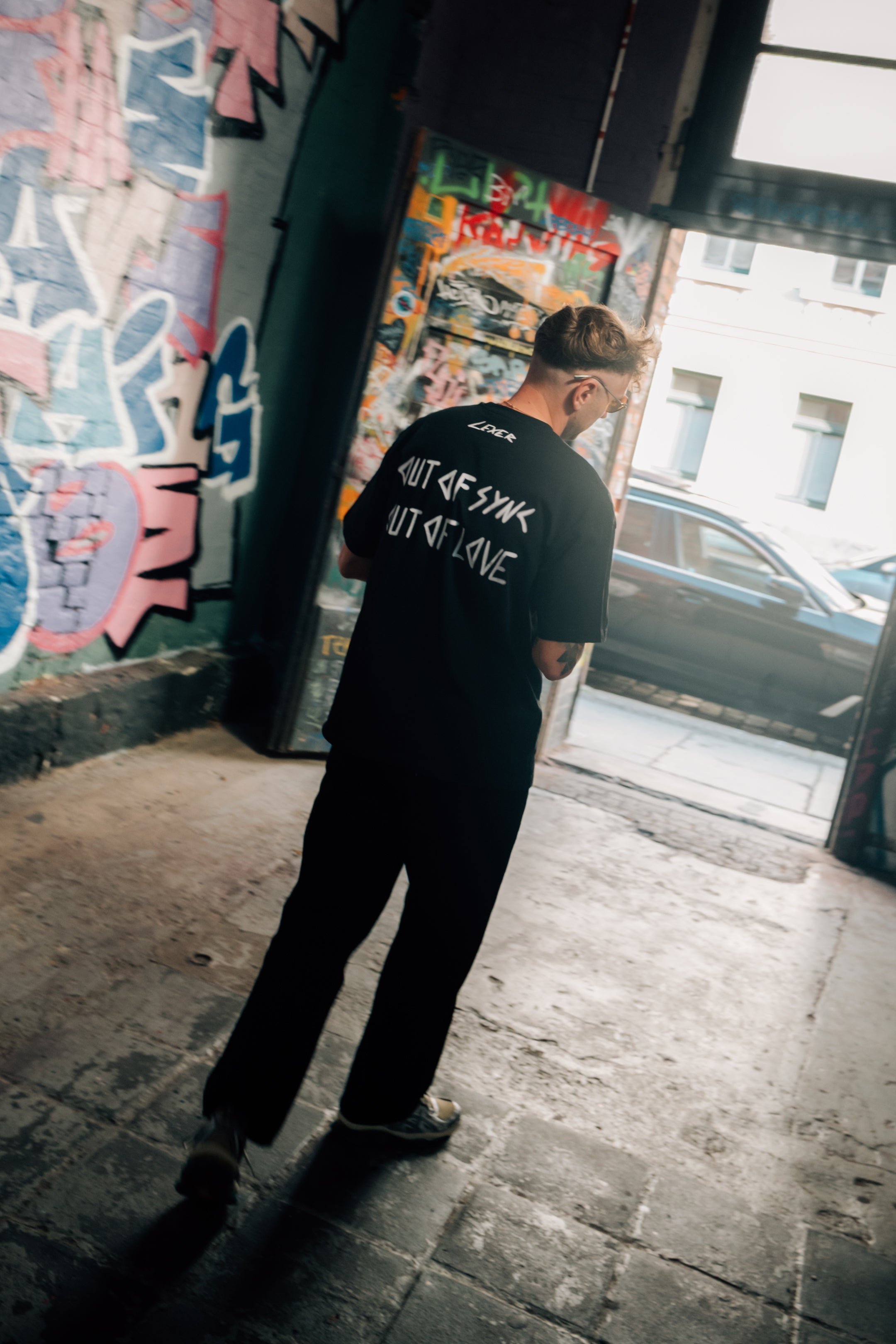 Schwarzes T-Shirt mit Commerz x Lexer Logo Out of Sync, Out of Love in Rosa Rückseite.